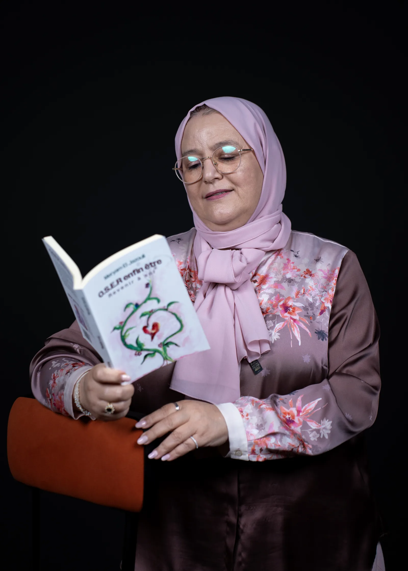 Meryam El Jazouli lisant O.S.E.R enfin être, assise dans un fauteuil coloré